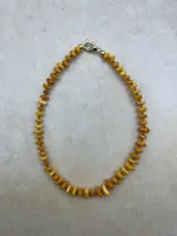 Collar corto tipo gargantilla compuesto por cuentas planas irregulares de ámbar en tonos amarillos y naranjas, separadas por pequeñas cuentas metálicas doradas. Cierre de mosquetón dorado.