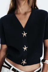Chaqueta azul marino de punto con escote pico y manga corta. Cierre frontal con tres botones dorados en forma de estrella.