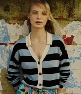 Cardigan de punto con cuello polo color crema, abotonado al frente con botones oscuros. Presenta un diseño de rayas horizontales anchas en azul celeste y negro.