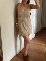 Vestido corto de tejido de punto color beige/dorado, con escote redondo y tirantes anchos. Presenta un tejido acanalado verticalmente con hilos de lurex que le dan brillo.