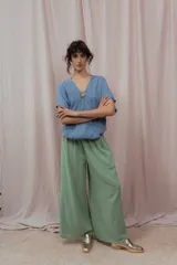 Blusa de lino color azul claro con escote en V cruzado y manga corta. Se ajusta en el centro del busto con un botón redondo de madera o metal con relieve.