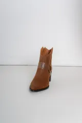 Bota corta de cuero color bordó, con taco cuadrado y punta fina. Presenta una correa con tachas pequeñas y una argolla metálica decorativa alrededor del tobillo. Cuenta con cierre lateral.