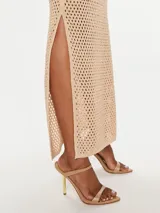 Vestido largo de tejido de punto color beige, con cuello halter y aberturas laterales. El tejido es calado con un patrón de pequeños rombos.