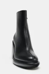 Botín negro de cuero sintético con cuña alta y punta redonda. Cierre con cremallera lateral.