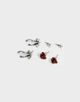 Set de tres pares de aros pasantes con cierre de tope a presión: un par de aros con forma de rosa color rojo óxido, un par de aros con forma de moño plateado y un par de aros con forma de perla blanca.