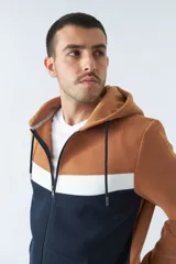 Campera con capucha color marrón, azul y blanco, con cierre frontal y bolsillos tipo canguro.