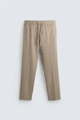 Pantalón color beige de corte recto, con cintura elástica ajustable con cordón. Tiene bolsillos laterales y traseros de vivo.