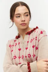 Cárdigan de punto color beige con cuello polo con volados azules, cierre frontal con botones y estampado de corazones y flores en azul y gris.