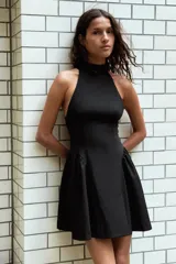 Vestido corto negro con cuello halter y sisas. Detalle de frunces en la falda. Cierre en la espalda con cremallera oculta.