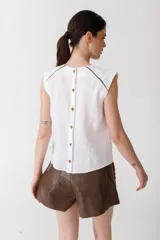Blusa color ladrillo de lino 100% con cuello redondo y sin mangas. Presenta vivos y pespuntes a contratono en color marrón.