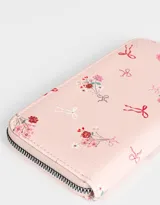 Billetera de cuerina color crema con estampado de flores y moños. Tiene formato rectangular, cierre circundante con tirador y múltiples compartimentos internos.
