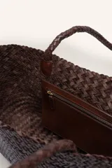 Bolso tipo tote de cuero vacuno, completamente trenzado a mano. El color es marrón oscuro, casi chocolate. Posee dos asas de hombro trenzadas.