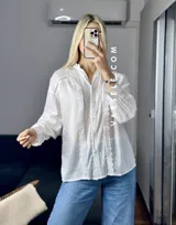 Camisa blanca de mangas largas con puños abullonados y detalles de encaje en cuello, mangas y ruedo.