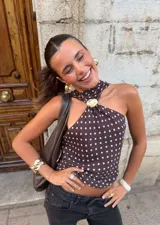 Top marrón con lunares blancos, de un solo hombro, con cuello halter y detalle de hebilla dorada.