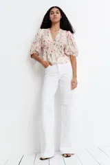 Blusa corta color blanco con estampado floral en tonos rosados y verdes. Presenta escote en V pronunciado, elásticos finos en la cintura y mangas globo cortas con elástico en los puños.