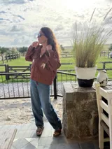 Campera bomber de jean color terracota, con corte holgado. Presenta apliques de cuero cortados y bordados a mano en la espalda, delantera y cuello, formando un diseño de montañas en tonos beige, rosa y verde militar.