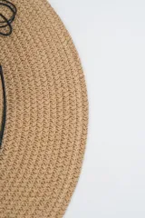 Sombrero de paja tejido color caqui, con ala ancha y copa tipo fedora. Está decorado con una cinta negra adornada con cuentas de madera, dijes turquesa en forma de hoja y dije de caracol.