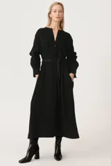 Vestido midi negro confeccionado en viscosa. Tiene cuello redondo con detalles deshilachados, manga larga con hombro caído y puños con pliegues. Cuenta con bolsillos laterales ocultos, trabillas y pliegue en la espalda.