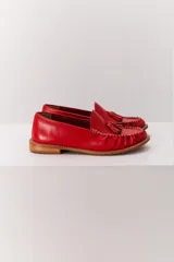 Mocasín de cuero color marrón claro, con detalle de flecos y borlas en la parte delantera. Diseñado en Uruguay y fabricado en Brasil.
