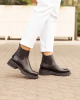 Botas Chelsea negras de cuero, con suela track y detalles de charol en la puntera y el talón.