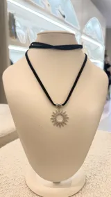 Gargantilla negra de gamuza con dije plateado en forma de sol con incrustaciones brillantes.