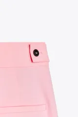 Pantalón rosa de tiro medio con trabillas en la cintura, bolsillos laterales, pinzas delanteras y pierna ancha. Cierre frontal con cremallera, botón y ganchos metálicos.