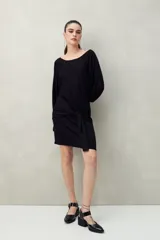Vestido corto negro de punto con brillo sutil, mangas largas amplias, falda ajustada y lazo frontal en la cintura.