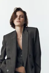 Blazer gris con diseño de líneas verticales, cuello solapa, manga larga con hombreras, bolsillos delanteros de vivo y cierre frontal cruzado con botones.