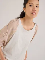 Remera gris de algodón con mangas color beige con bordados de líneas en blanco, amarillo y gris.