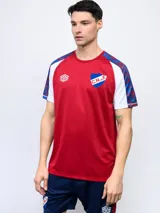 Remera de entrenamiento Umbro del Club Nacional de Football. Diseño rojo con mangas raglán blancas con estampado azul y rojo. Incluye logo de Umbro y escudo del club en el frente.
