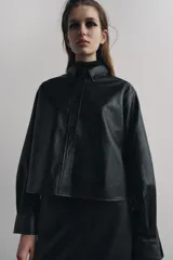 Sobrecamisa negra de efecto piel, con cuello de solapa, manga larga con puños abotonados, bajo recto y cierre frontal con botones.