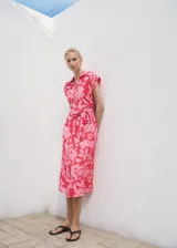 Vestido midi de manga corta con cuello camisero y cierre de botones frontal. Presenta un estampado floral en tonos rosados y un cinturón ajustable a juego.