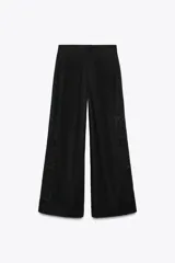 Pantalón negro con bordados florales en los laterales, tiro alto, cintura elástica en la parte trasera, bolsillos laterales, pliegues y cierre frontal con cremallera, botón interior y gancho metálico.