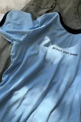 Remera blanca de algodón con ribete amarillo en cuello y mangas, y frase bordada en color naranja.