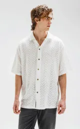 Camisa blanca de manga corta con textura calada y cierre con botones marrones.