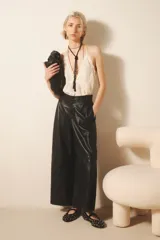 Pantalón ancho de cuero ovino color negro, con pinzas delanteras, cierre con snaps metálicos y tiras ajustables en la cintura.