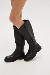 Bota alta de caña ancha color negro, con cierre lateral y detalle de hebilla ajustable en la parte superior de la caña. Suela de goma gruesa con relieve.