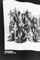 Camiseta blanca de algodón con cuello redondo y mangas cortas. Estampado fotográfico en blanco y negro con un grupo de personas y texto "Steven Meisel NYC February 12, 2025".