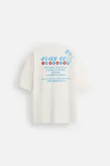 Camiseta color crudo de corte relaxed fit, cuello redondo y manga corta. Estampado frontal con texto "Flies to Los Angeles CA" y diseño de bandera a cuadros.