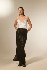 Falda larga negra de corte tubo, cubierta completamente de lentejuelas brillantes. Presenta una abertura lateral en la pierna.