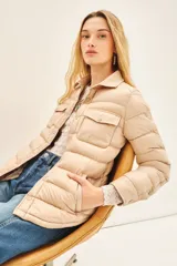 Campera puffer color beige con cuello camisero, cierre con botones a presión, bolsillos con solapa en el pecho y relleno de plumas.
