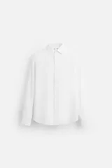 Camisa blanca de corte slim fit, confeccionada en algodón, con cuello italiano, mangas largas con puños abotonados y cierre frontal con botones.