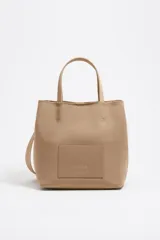 Bolso de mano Bimba y Lola modelo Chihuahua L, color beige, con doble asa de mano y asa de tejido. Presenta logo metálico y bolsillo interior con cierre de cremallera.