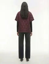 Poncho acolchado color mostaza con cuello alto y abertura frontal con cierre. Presenta un patrón capitoné de formas ovaladas y bolsillos delanteros.