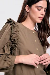 Blusa color verde militar con cuello redondo, abotonada al frente y mangas largas abullonadas con volados en los hombros.