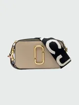 Bandolera Marc Jacobs modelo The Snapshot, color beige con logo dorado y correa ancha de tela negra con letras blancas.