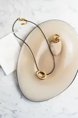 Collar con cordón negro y dije dorado con forma de doble aro entrelazado.