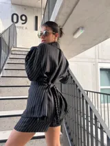 Blazer negro a rayas verticales blancas, con solapas de muesca, cierre cruzado con botones y corte entallado.