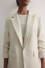 Blazer color crema con solapas de muesca, mangas tres cuartos fruncidas y bolsillos delanteros con solapa. Sin cierre. Forrado.
