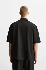 Sobrecamisa color beige de tejido elástico, con cuello solapa, manga corta y bolsillos de parche en el pecho. Cierre frontal con botones a presión.